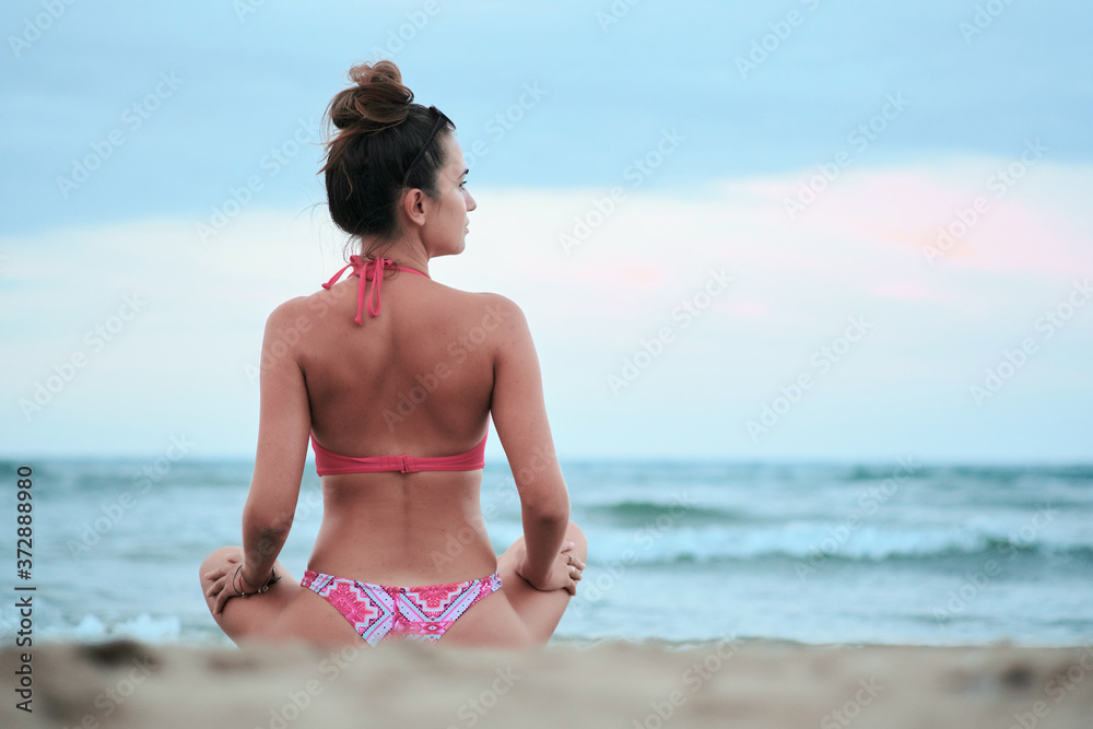 The girl sits on the sand by the sea and the view from the back. Girl in a pink swimsuit The girl sits on the sand by the sea and the view from the back. Girl in a pink swimsuit
