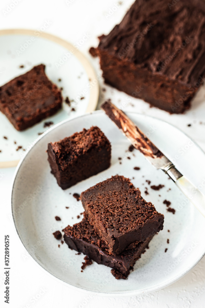 Sliced chocolate loaf cake served on two plates, a knife covered with chocolate, high key, white background