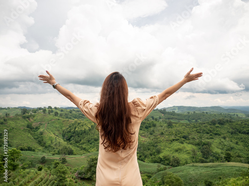 happy Asian woman standing and open arms on hill with green mountain view in background. Nan, Thailand.
