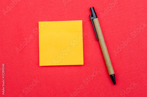 Yellow sheet of writing paper, ballpoint pen on red background, copy space, top view