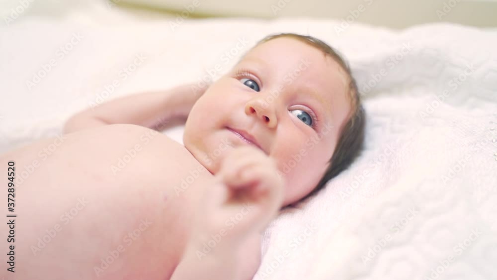 close-up portrait a young newborn girl. The face of a Caucasian little girl with blue eyes, lying on the bed, showing his tongue, and waving his arms. baby 1 mounth looking in camera. child relaxing close-up portrait a young newborn girl. The face of a Caucasian little girl with blue eyes, lying on the bed, showing his tongue, and waving his arms. baby 1 mounth looking in camera. child relaxing