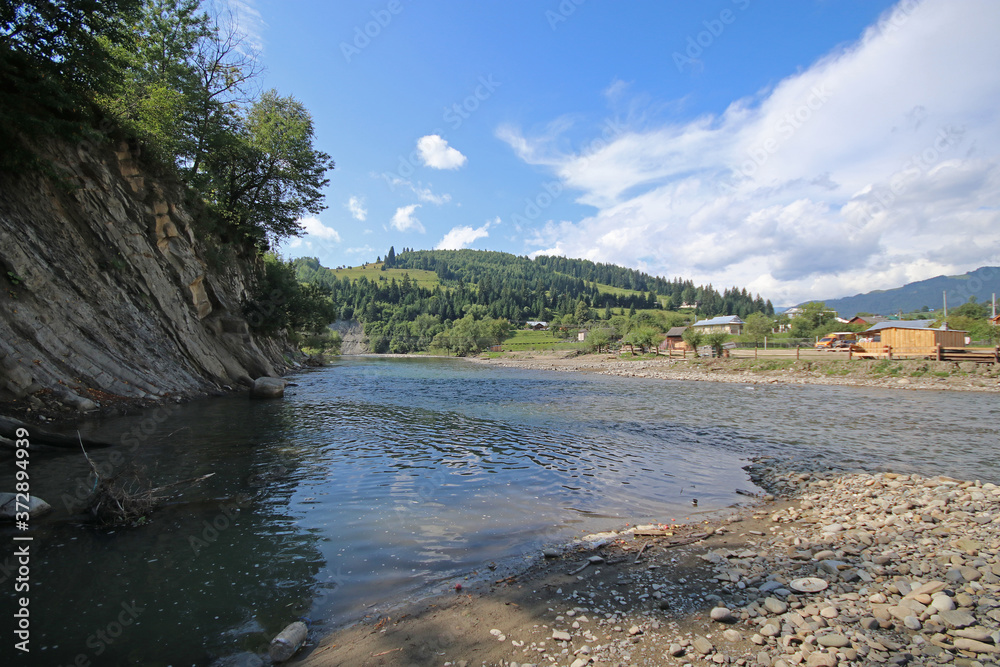 Mountain river with clear water, mountains, forest and a village on the other side of the river. Carpathians, Ukraine.