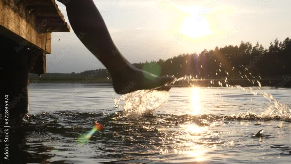 Persons feet splashing water at the sunset. Enjoying holidays by lake