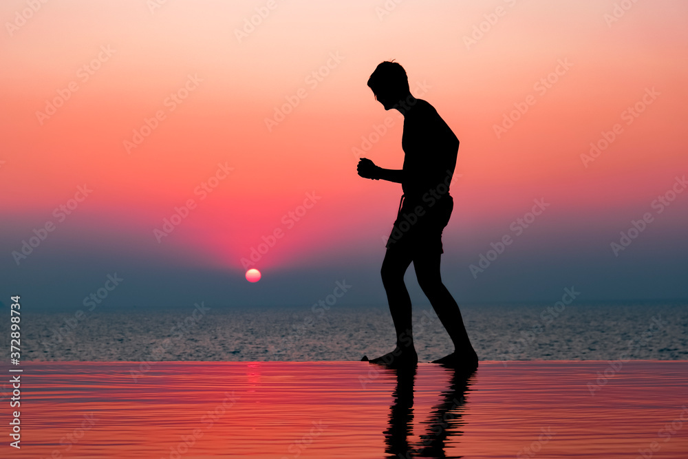 Young man in a pool enjoying the sunset. Human silhouette over the setting sun. Swimming pool in the evening. Young man in a pool enjoying the sunset. Human silhouette over the setting sun. Swimming pool in the evening.
