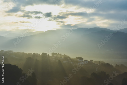 Sunrise in a misty place, with the sunrays casting the shadows of mountains, houses and trees