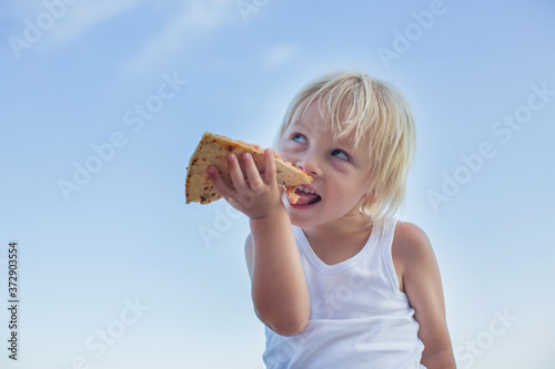 Sweet toddler child, eating pizza on the beach, having fun, smiling happily, kid enjoying dinner