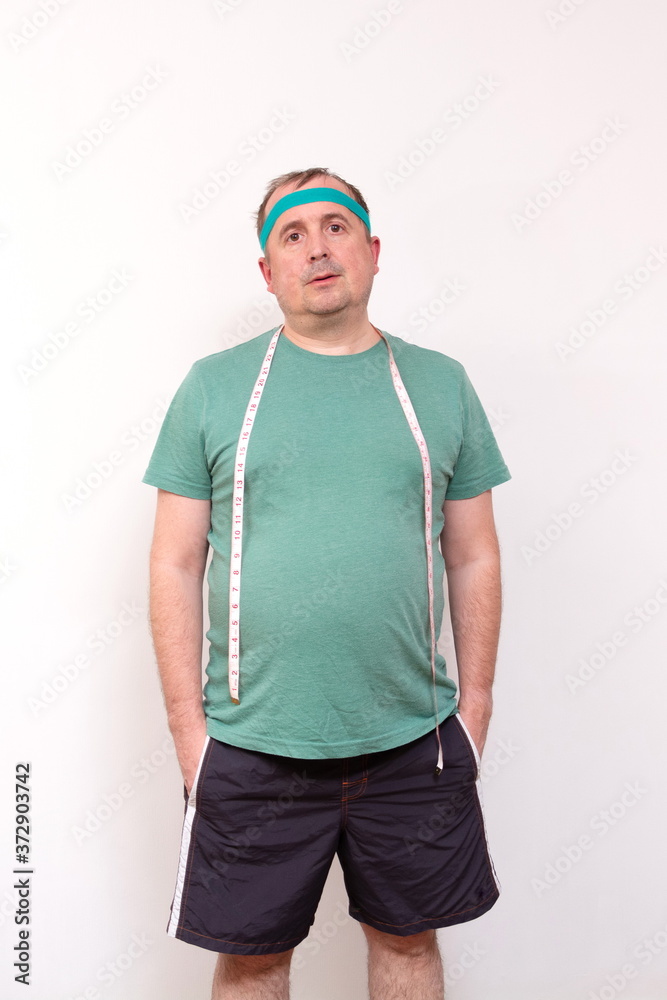 A funny fat man in a green bandana and a t-shirt with a measuring tape around his neck. half-length portrait. home fitness training, independent training. A funny fat man in a green bandana and a t-shirt with a measuring tape around his neck. half-length portrait. home fitness training, independent training.