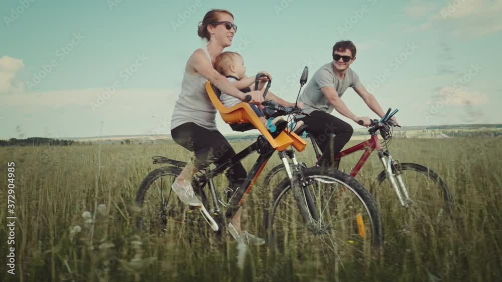 Family cycling outdoor. Young family cycling with baby on a green summer field.