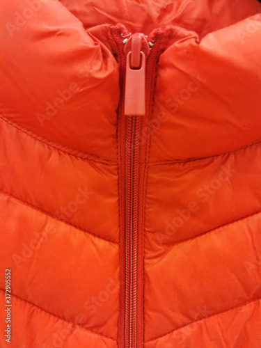 Close-up on orange puffer jacket texture with a zipper and a runner close-up