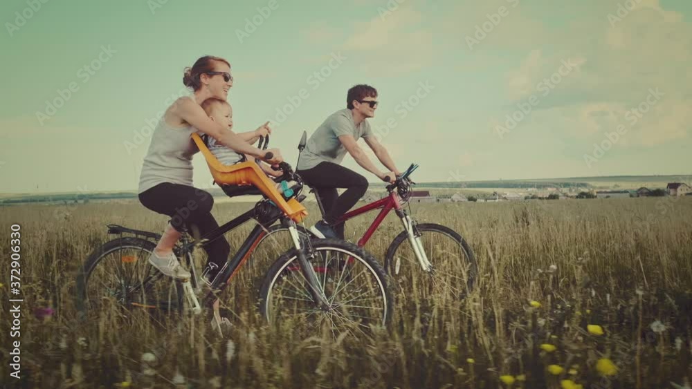 Family cycling outdoor. Young family cycling with baby on a green summer field. Family cycling outdoor. Young family cycling with baby on a green summer field.