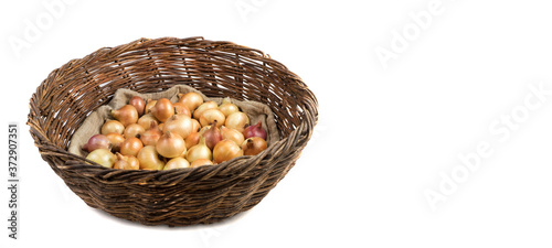 Collecting yellow and pink onions on a linen bag in a basket of vines isolated on a white background, side view. Full frame, Panorama. Vegetable background. Concept of food, farm products.