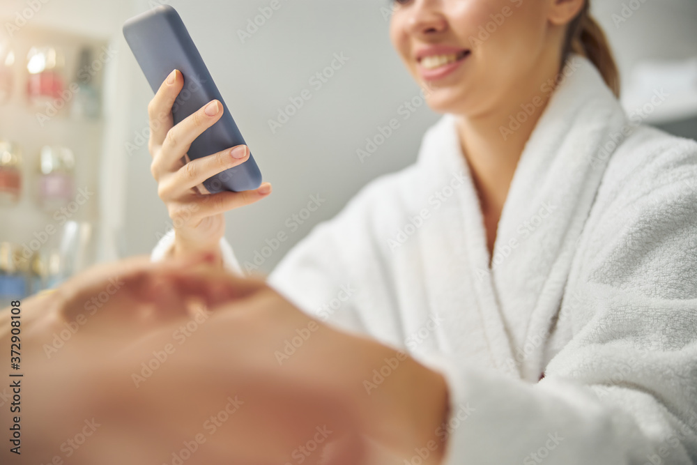 Cheerful young woman using smartphone during manicure Cheerful young woman using smartphone during manicure