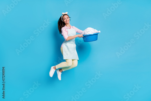 Fototapeta Naklejka Na Ścianę i Meble -  Full length body size view of her she nice attractive pretty cheerful glad girl maid jumping holding in hand making laundry bowl isolated on bright vivid shine vibrant blue color background
