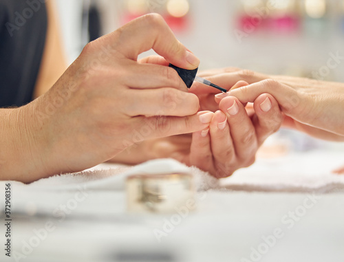 Beautician applying enamel on client fingers in salon