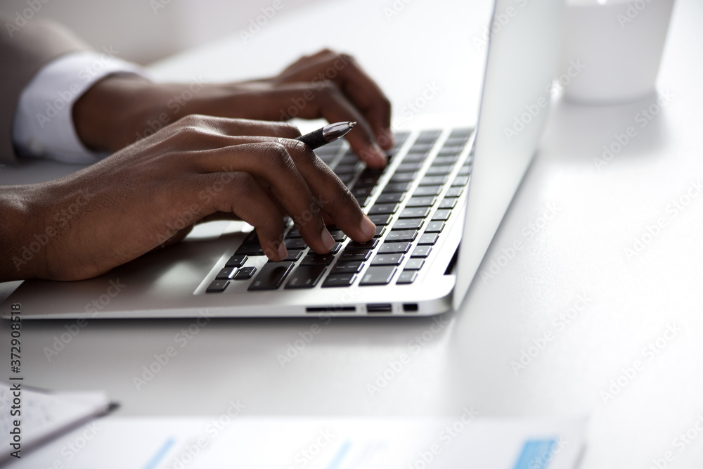 Close-up of hands of african-american businessman typing on a laptop.