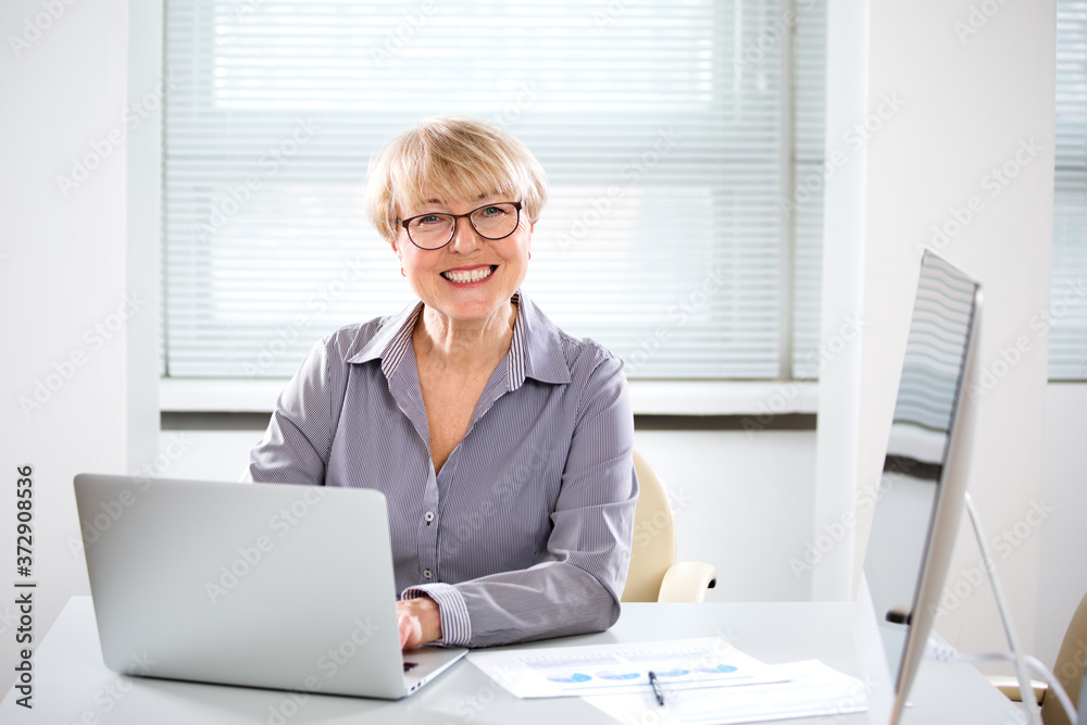 Portrait of mature business woman looking at camera in an office - obrazy, fototapety, plakaty 