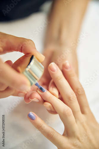 Beautician painting woman finger nails in blue