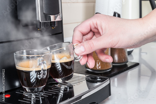 in two cups of glass of coffee Prepared on the coffee machine. A woman's hand picks up an espresso Cup