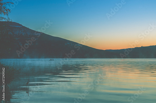 Dawn over a large mountain lake covered with fog against the backdrop of mountain peaks.