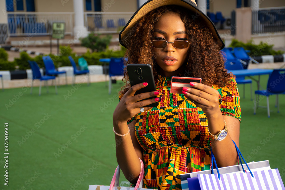 young african woman using her phone and credit card outdoor - obrazy, fototapety, plakaty 