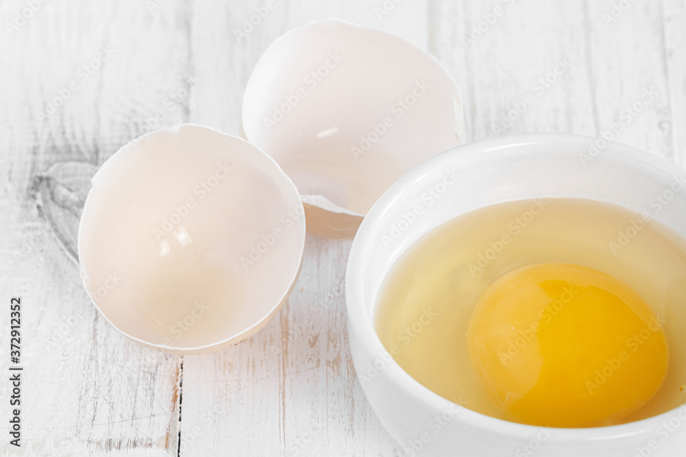 Row fresh egg in ceramic small white plate and two parts of shell on painted wooden background horizontal macro Row fresh egg in ceramic small white plate and two parts of shell on painted wooden background horizontal macro