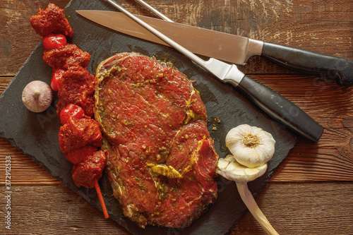 Slice of spiced beef with bbq skewer of beef and tomato with garlic knife and fork on slate plate on wooden table