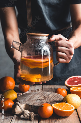 A man pours citrus tea on a wooden table. Healthy drink, vintage style. Vegan, eco products.