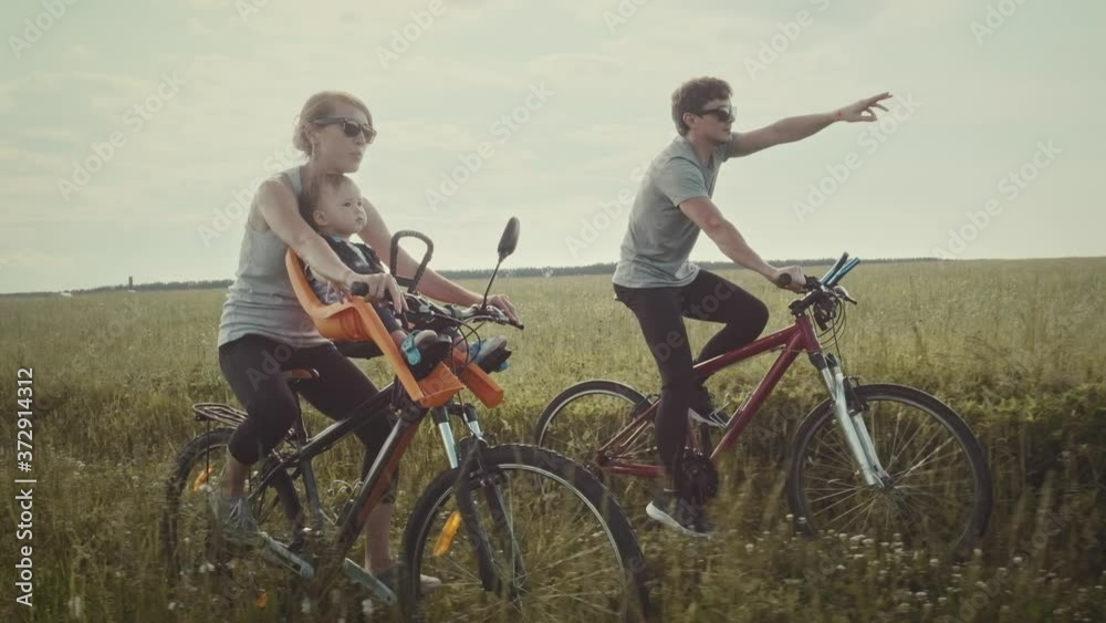 Family cycling outdoor. Young family cycling with baby on a green summer field. Family cycling outdoor. Young family cycling with baby on a green summer field.