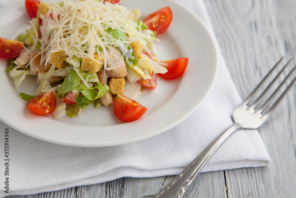 Tasty Caesar salad in a white plate on a wooden background. Close up. Tasty Caesar salad in a white plate on a wooden background. Close up.