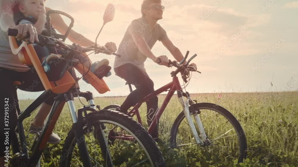 Family cycling outdoor. Young family cycling with baby on a green summer field. Family cycling outdoor. Young family cycling with baby on a green summer field.