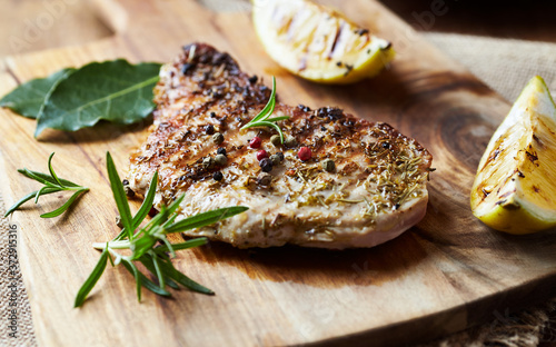 Grilled pork steak with fresh rosemary on wooden background.	