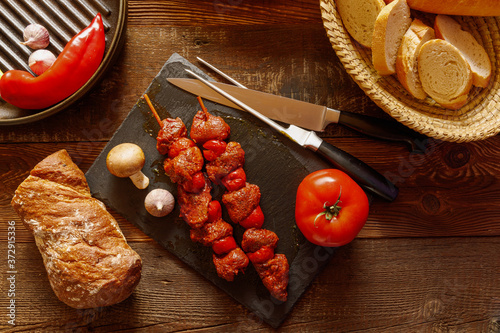 bbq skewer of beef and tomato on slate plate with garlic and mushroom bread in basket chilli pepper and cast-iron grill pan