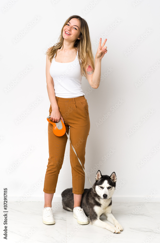 A full length young pretty woman with her dog showing victory sign with both hands A full length young pretty woman with her dog showing victory sign with both hands