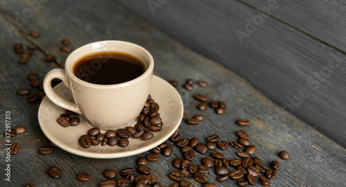 Coffee cup with roasted coffee beans on wooden table background. Mug of black coffe with scattered coffee beans on a wooden table. Fresh coffee beans.