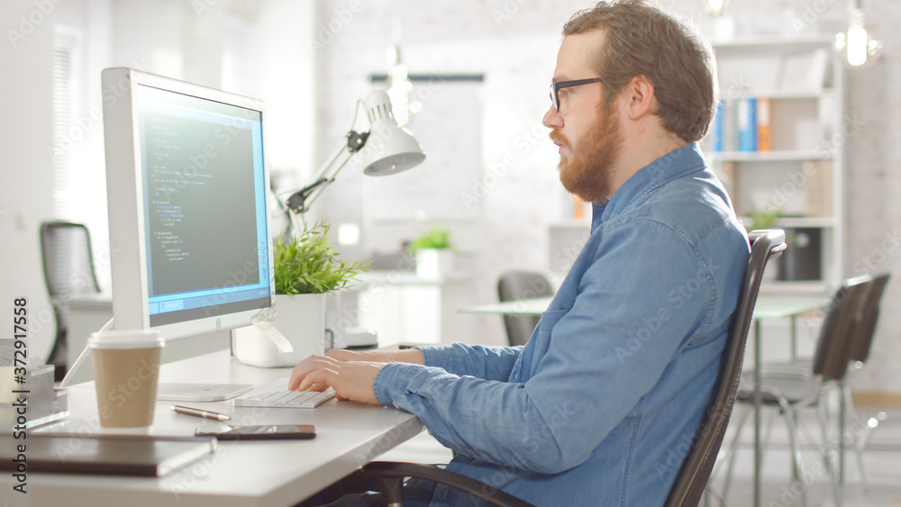 Bearded Creative Software Developer Works on Code While Sitting at His Desk. He is Working in Bright Modern Office.