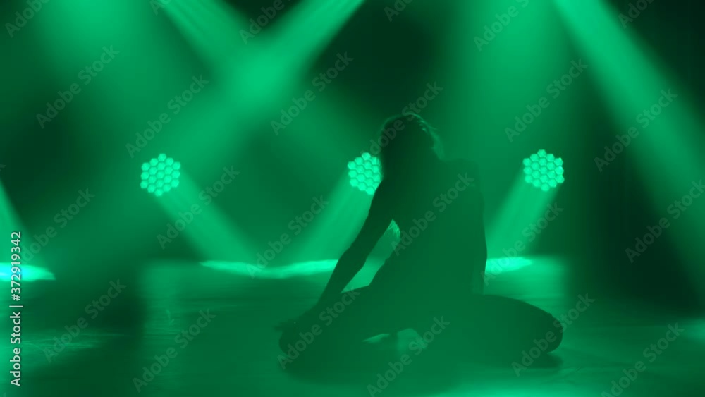 Silhouette dancing woman in tight fitting clothes in the dark room. A sexy female dancer performs erotic dance, strip plastic. Green spotlights and black background. Slow motion. Close up. Silhouette dancing woman in tight fitting clothes in the dark room. A sexy female dancer performs erotic dance, strip plastic. Green spotlights and black background. Slow motion. Close up.