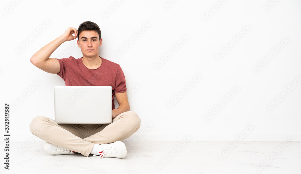 Teenager man sitting on the flor with his laptop with an expression of frustration and not understanding