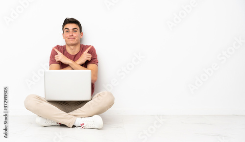 Teenager man sitting on the flor with his laptop pointing to the laterals having doubts © luismolinero