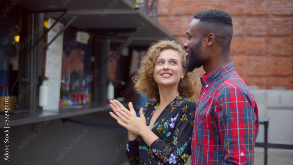 Obraz premium Young multiethnic couple choosing meal standing near food truck on street