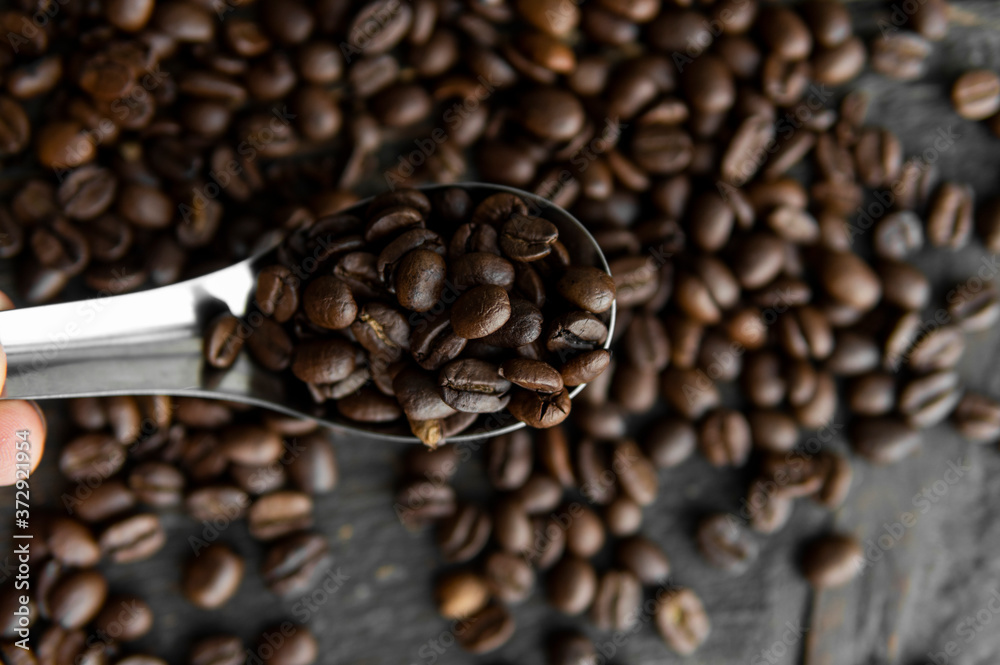 Obraz premium Fresh roasted arabica coffee beans in a metal spoon and scattered coffee beans on a wooden table.