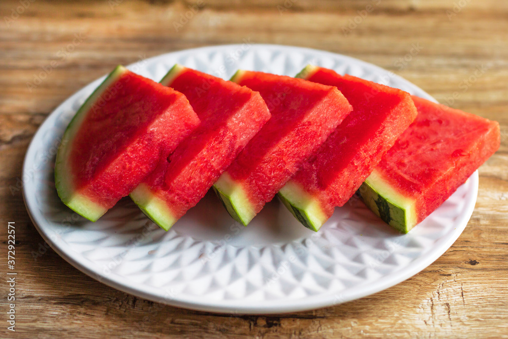 Slices of fresh ripe watermelon, cut in pieces on white plate on wooden background Slices of fresh ripe watermelon, cut in pieces on white plate on wooden background