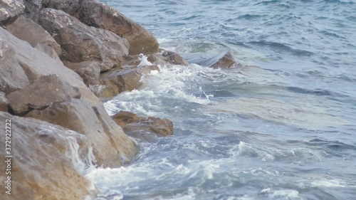 The waves hit the rocky sea shore. Cloudy overcast summer day. Handheld slow motion shot.
