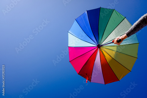 Woman holds a multicolored parasol on a summer day with blue sky background.