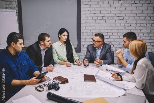 Male and female professional architects with experienced director sitting at one table during board meeting and discussing new sketches of building planning on own entrepreneurship.Mock up area