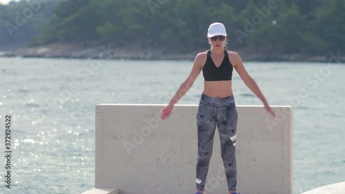 A woman in sportswear stretches after exercising on the beach by the sea. Sunny summer morning. Slow motion shot.
