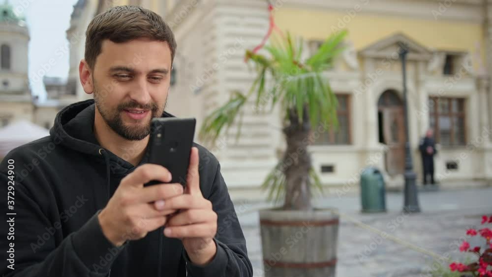 Portrait of guy making video call. Happy male having chat outside. Excited man looking phone screen outdoors. Blurred background. Portrait of guy making video call. Happy male having chat outside. Excited man looking phone screen outdoors. Blurred background.