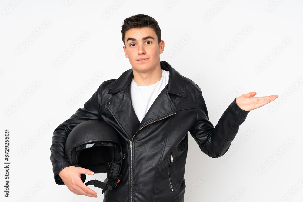 Man holding a motorcycle helmet isolated on white background having doubts with confuse face expression Man holding a motorcycle helmet isolated on white background having doubts with confuse face expression