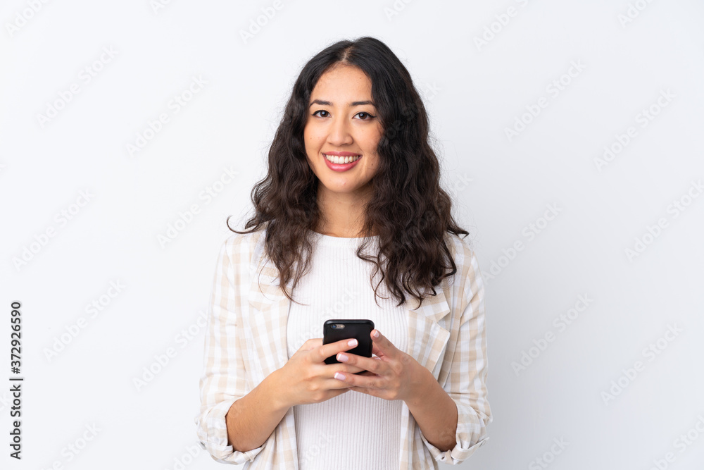 Mixed race woman over isolated white background sending a message with the mobile Mixed race woman over isolated white background sending a message with the mobile