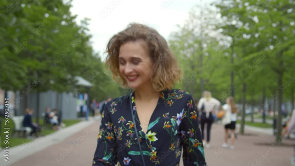 Young happy woman in dress walking along alley in city park Young happy woman in dress walking along alley in city park