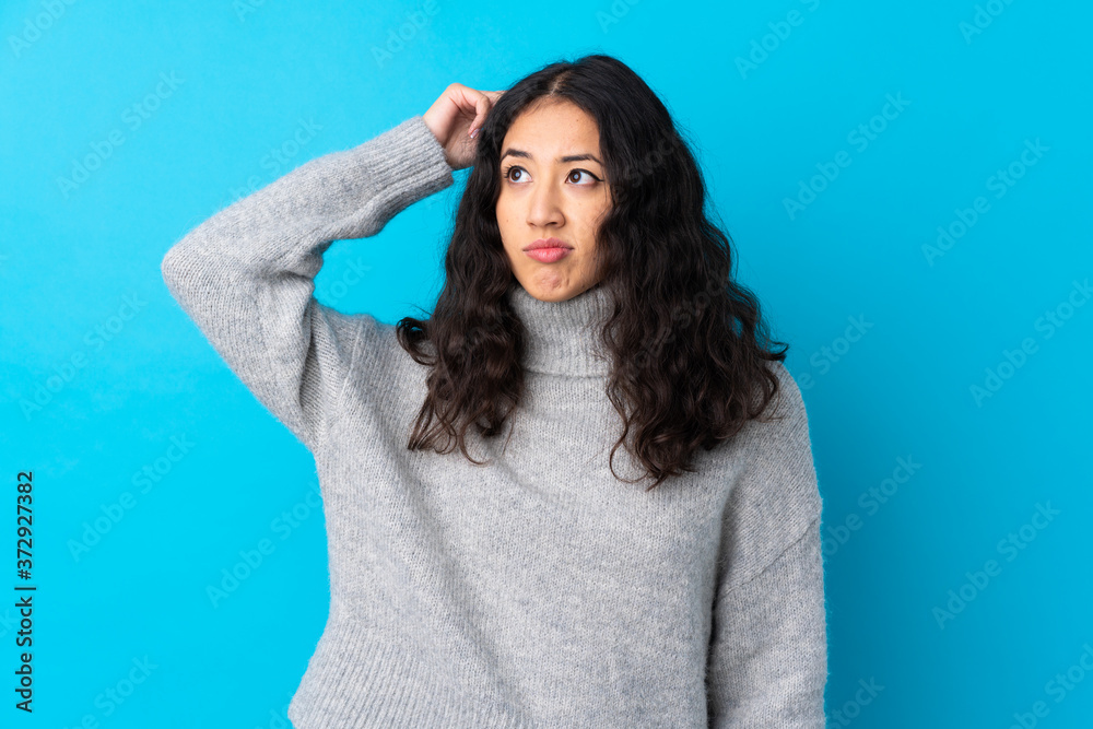 Fototapeta premium Spanish Chinese woman over isolated blue background having doubts while scratching head